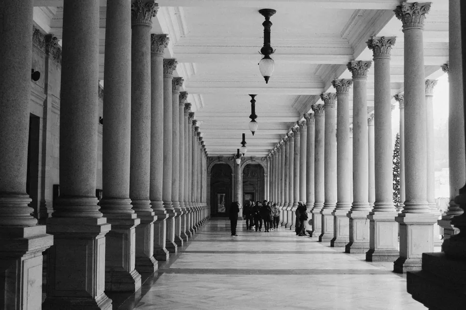 Columnata de un edificio institucional, con las columnas en perspectiva y figuras al fondo.